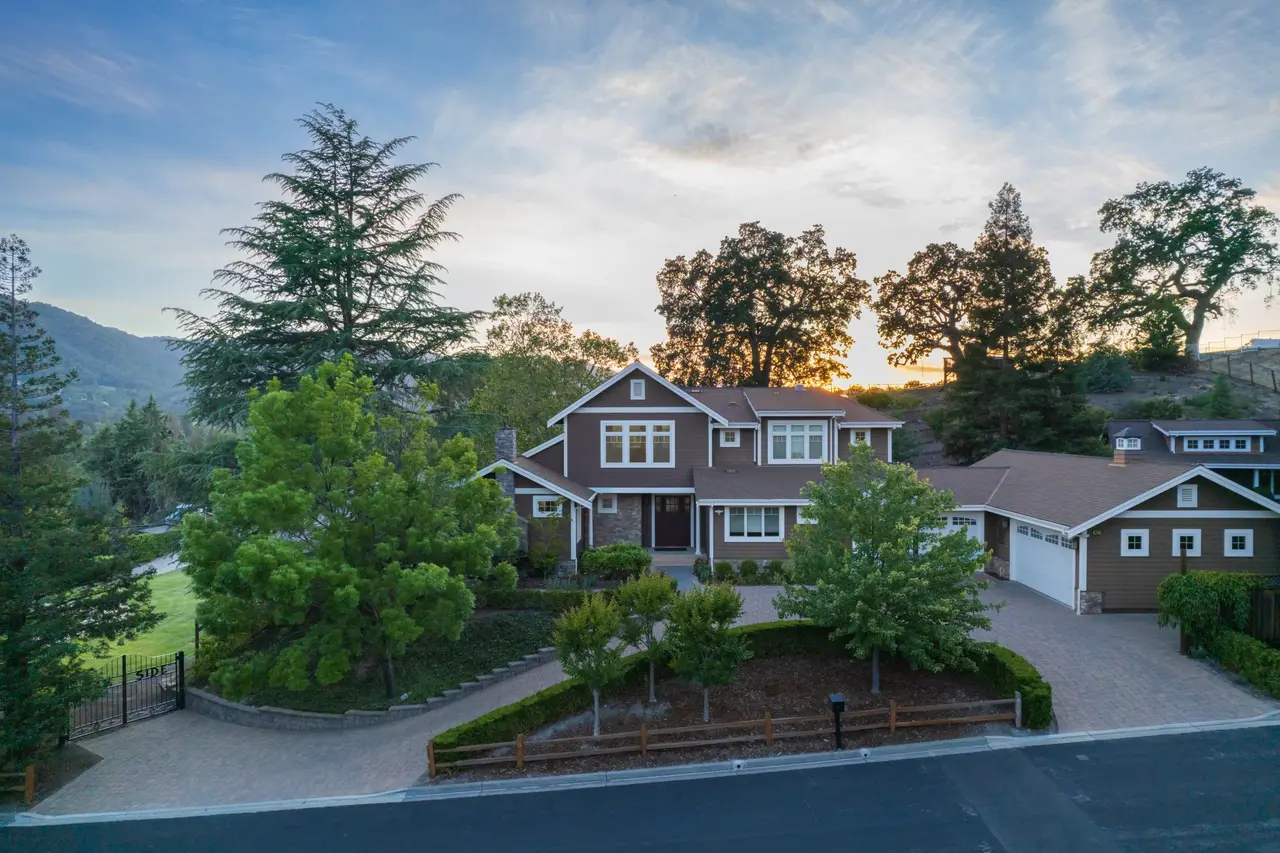 Two-story Craftsman home at sunset with a circular paver driveway and mature trees