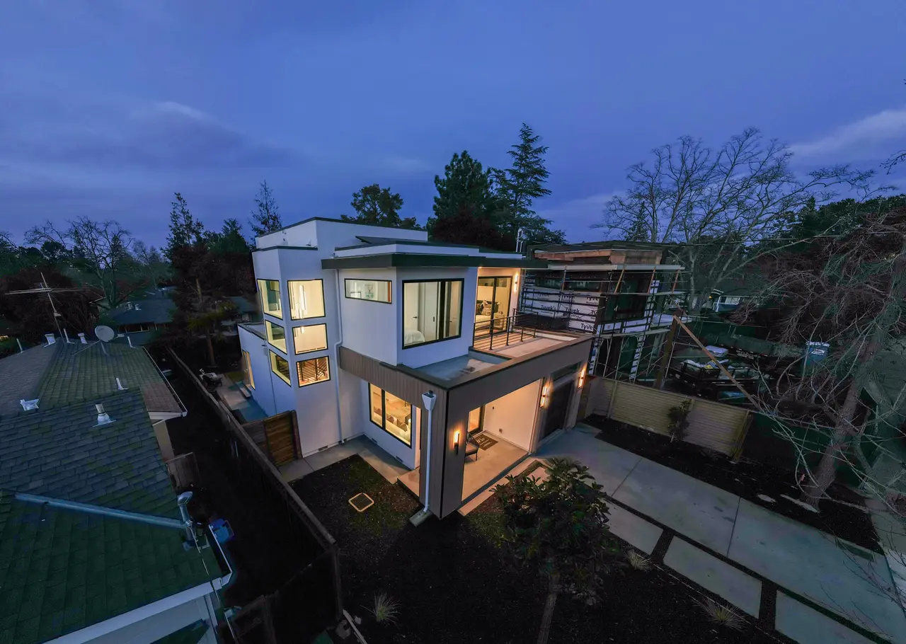 Aerial view of the home at twilight with glowing windows and an upper deck