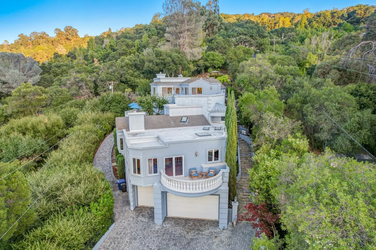 Daytime aerial of the home, its curved balcony, and the paver motor court