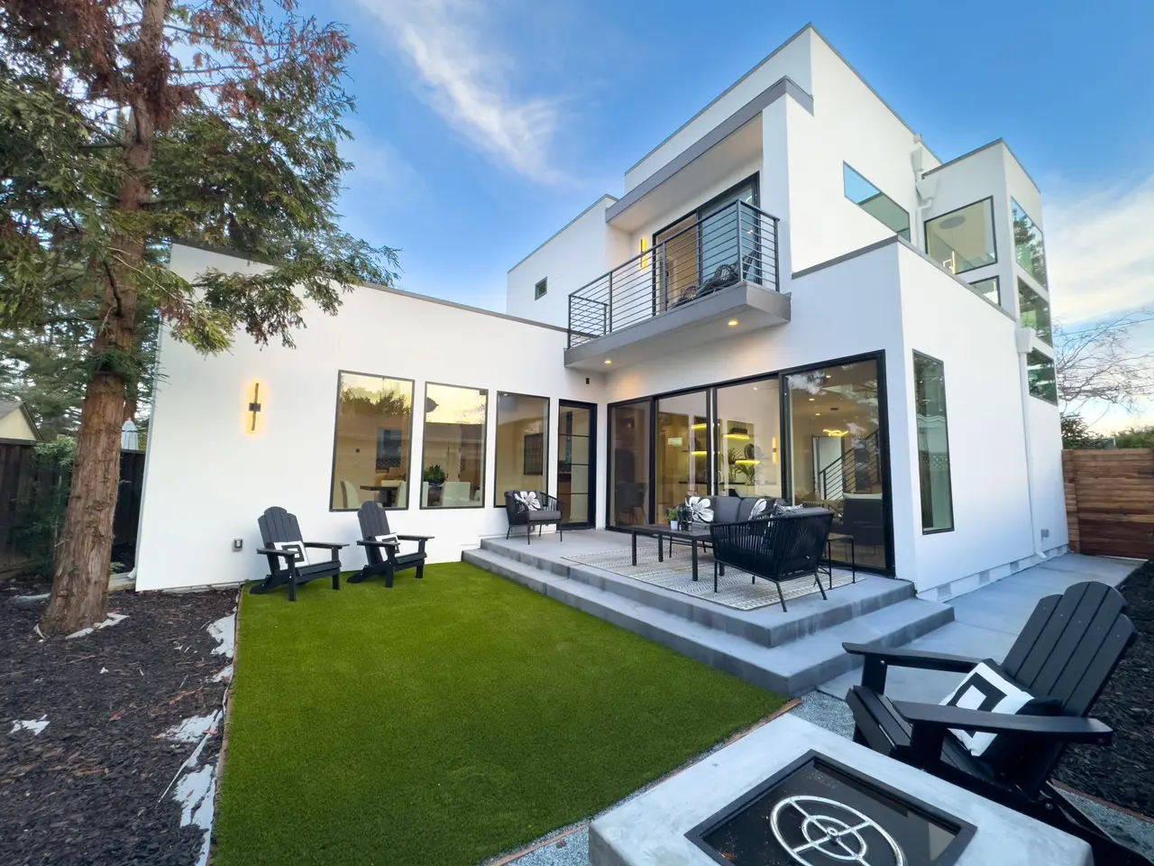 Backyard with a lawn, patio seating, and a fire pit below a balcony