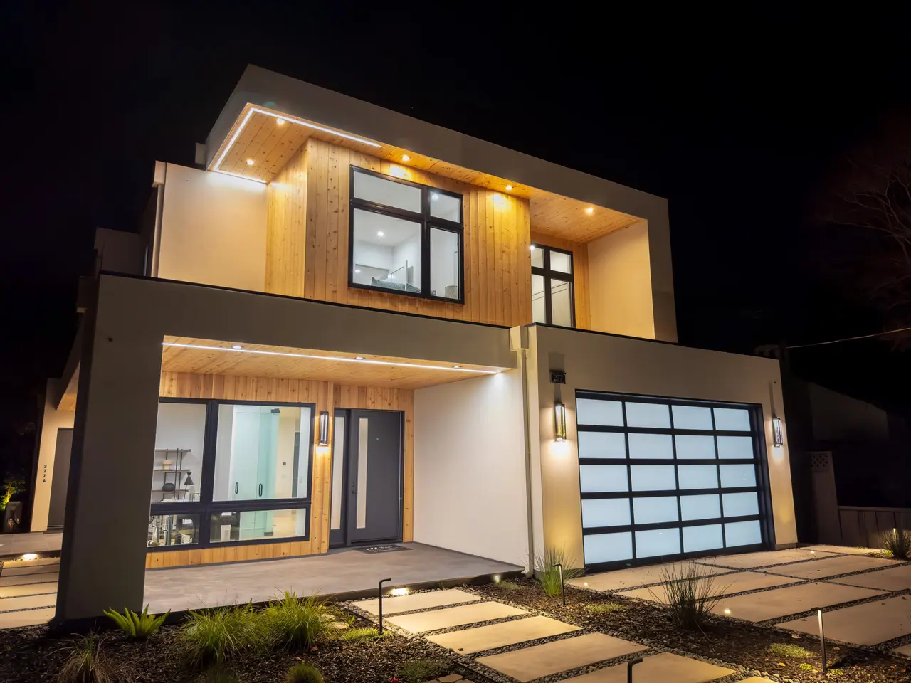 Angled night view of the front entry with warm wood soffits and wall sconces