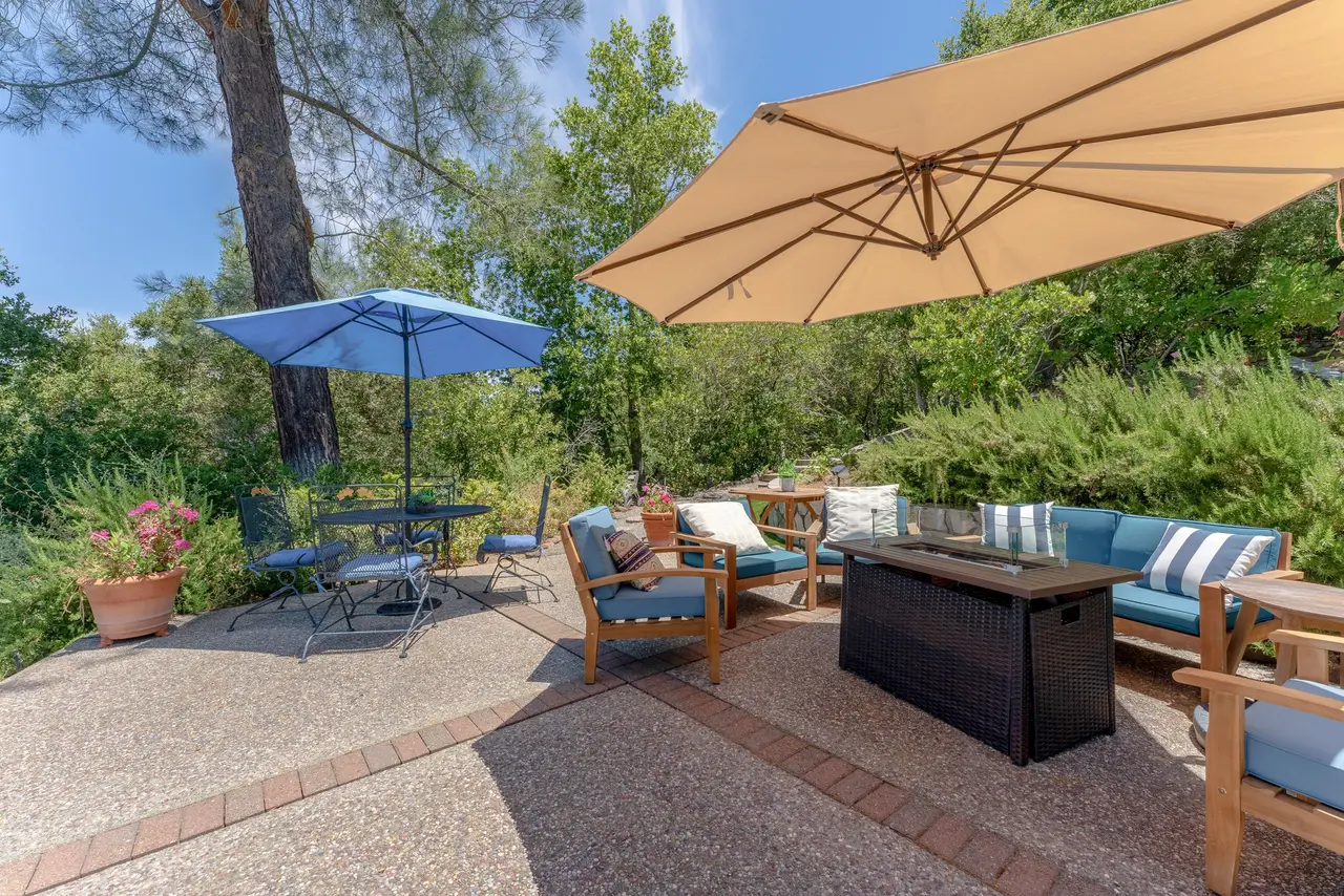 Shaded patio with umbrellas, lounge seating, and a fire table