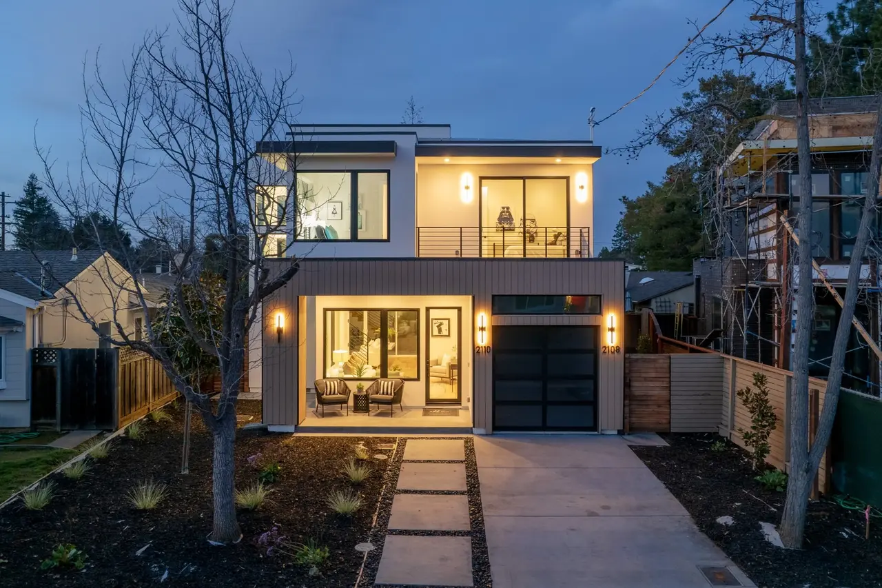 Street view at dusk with a lit front porch and a paver path